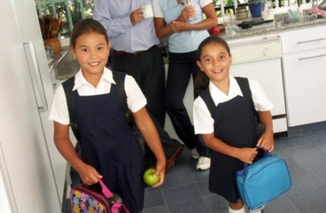 Children ready for school with lunchboxes and parents in background