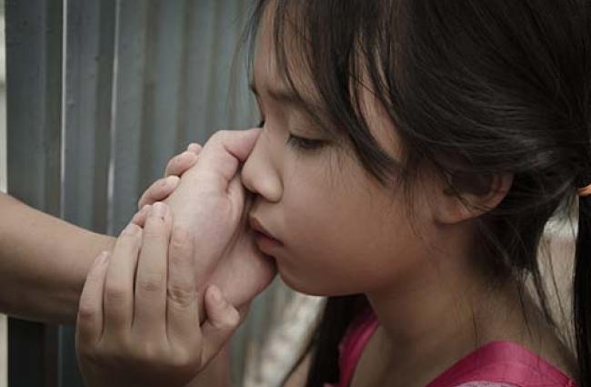 Child with parents hand on their cheek. Parent appears behind bars