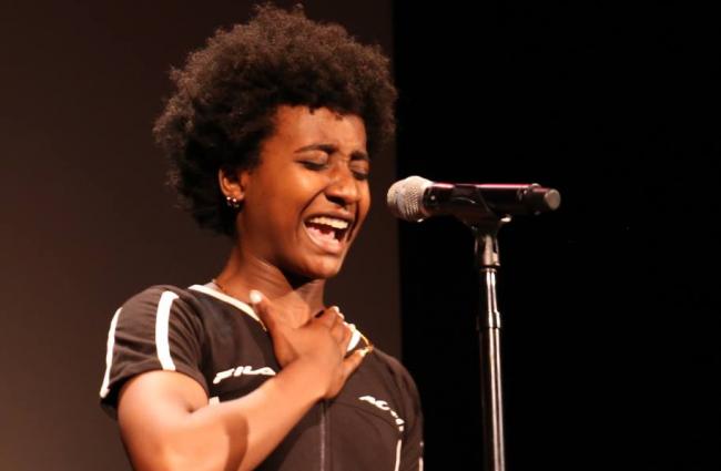Young African American woman passionately speaking into a microphone on stage.