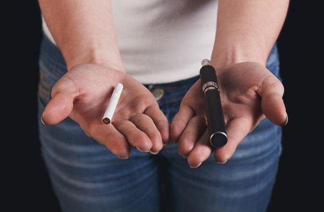 Image of a woman with a regular cigarette in one hand and an e-cigarette in the other.