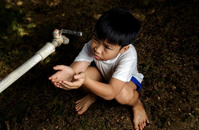 Image of a boy with his hands cupped under a spigot.