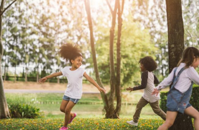 Image of children running and playing outside in a park with green grass and trees.
