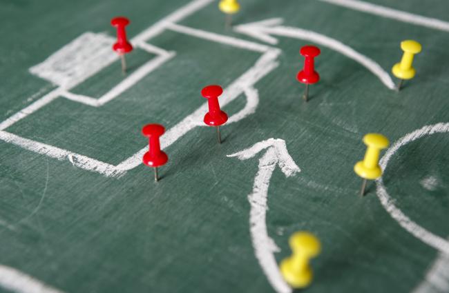 Red and yellow pushpins representing opposing soccer players on a game board, planning a play