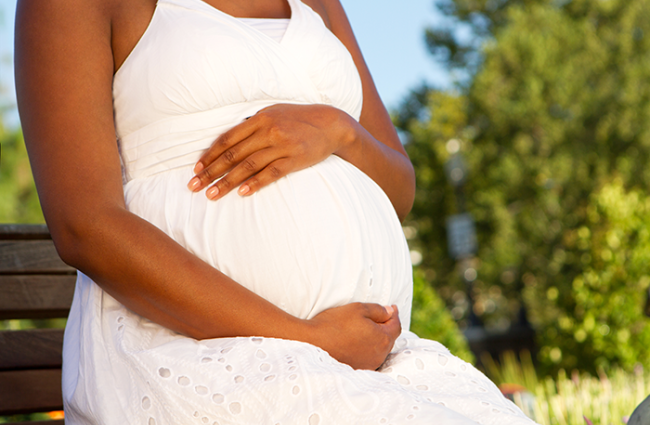 Pregnant person holding abdomen while sitting on what appears to be a park bench