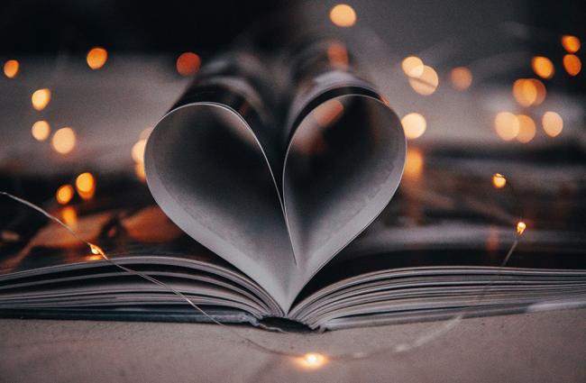 Book open with pages forming a heart, surrounded by fairy lights