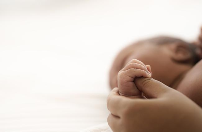 Black presenting infant holding the thumb of a Black presenting adult