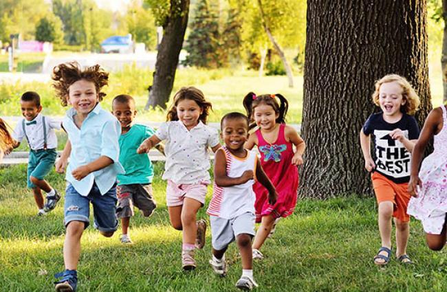 Diverse group of kids running on the grass toward the camera smiling