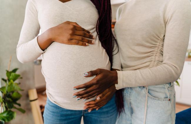 An LGBTQ+ couple that shows from the chest down to the waist, holding each other while one is pregnant