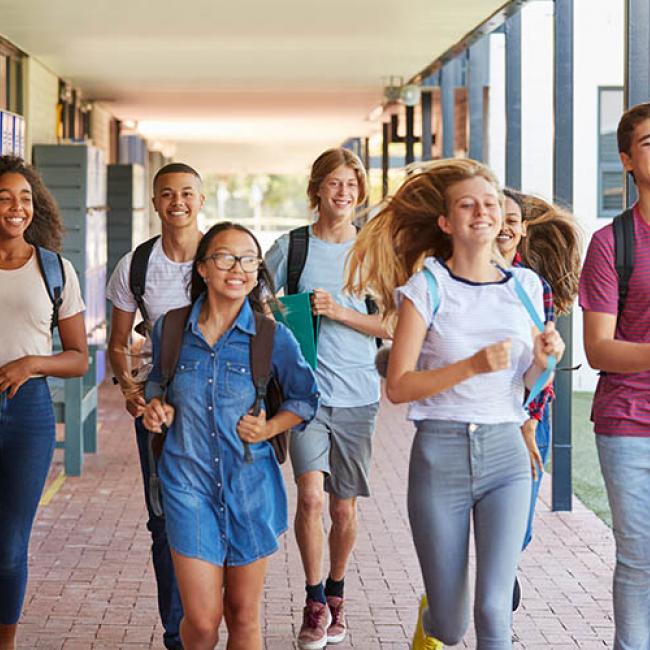 Students smiling and running towards camera thru a school corridor