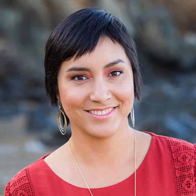 Smiling woman with short black hair, dangling ears, a thin necklace, and a red top