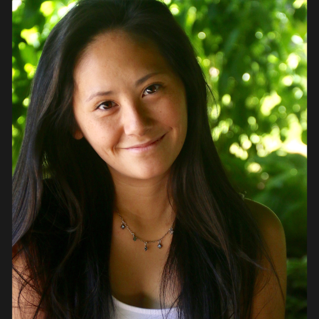 Elissa Carey, a smiling Chinese American woman with long dark hair. She's wearing a dangly beaded necklace and white top. She's sitting in front of a green leafy background.