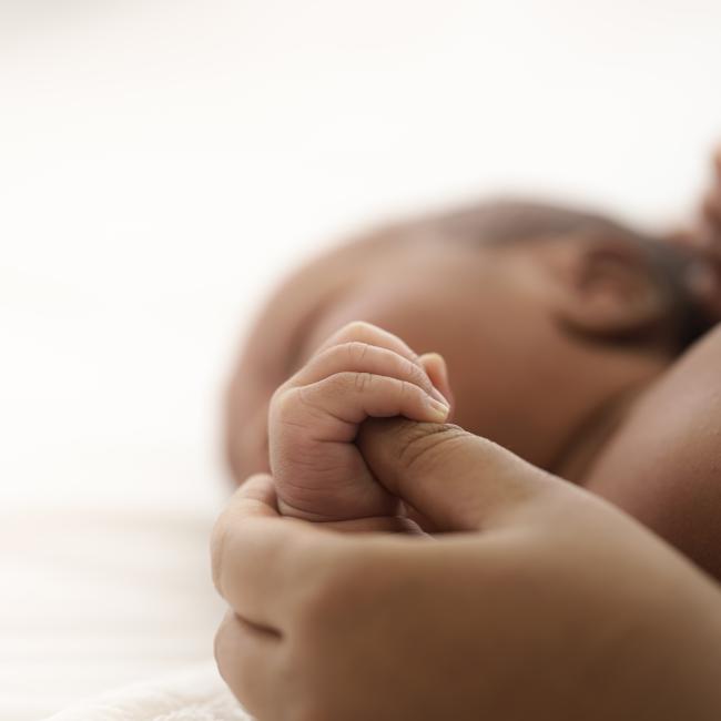 Close up of Black infant holding a Black person's thumb