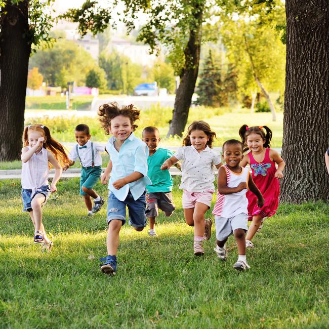 Diverse group of kids running on the grass toward the camera smiling