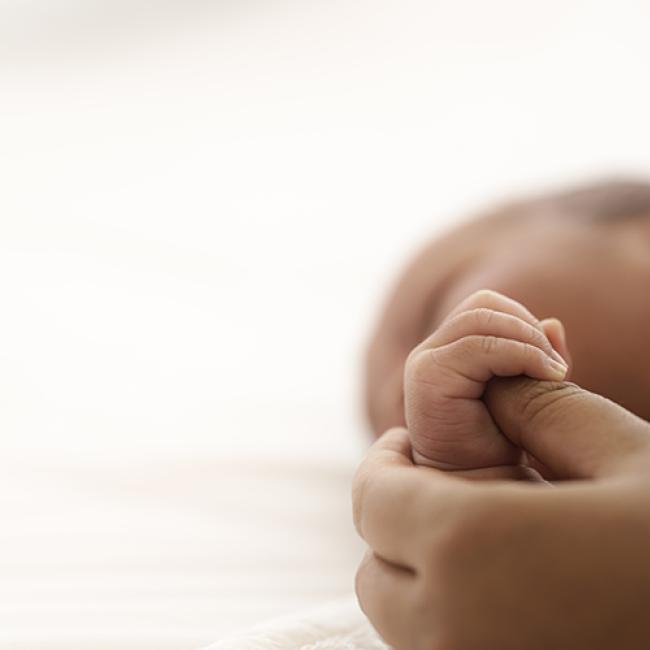 Black presenting infant holding the thumb of a Black presenting adult