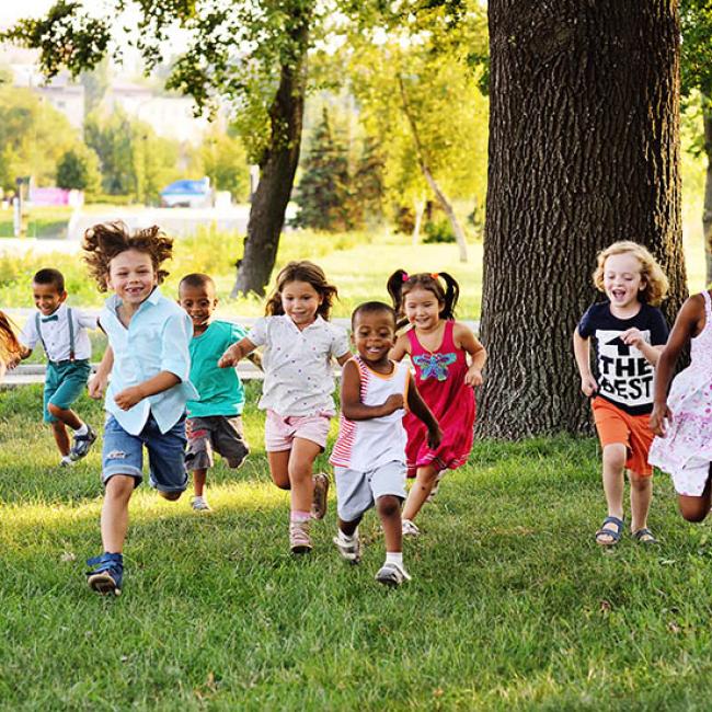 Diverse group of kids running on the grass toward the camera smiling