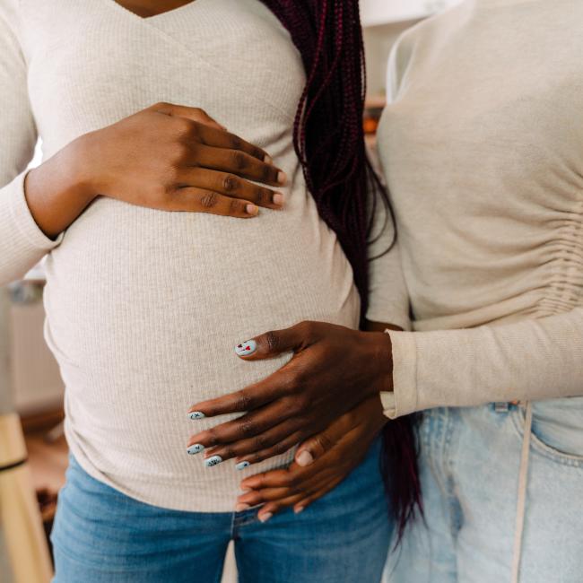 An LGBTQ+ couple that shows from the chest down to the waist, holding each other while one is pregnant