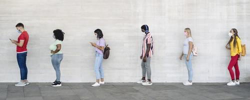Line of people socially distanced and wearing masks in front of a white wall