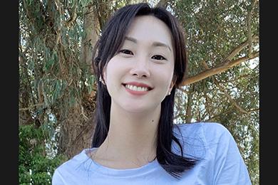 Dr. Ye Ji Kim, a dark-haired Korean American female-identifying epidemiologist wearing a light blue top and standing in front of a tree 