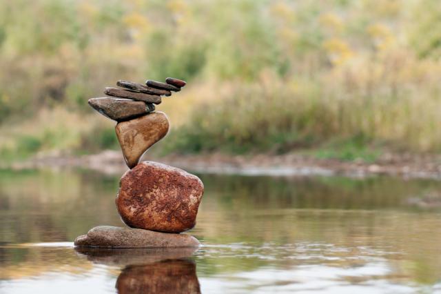 Precarious looking stack of rocks in a lake with grasses in the background.